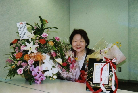 田内理事長からの花かご、京都の会から届いた花束、盾に囲まれて満面の笑みの理事長