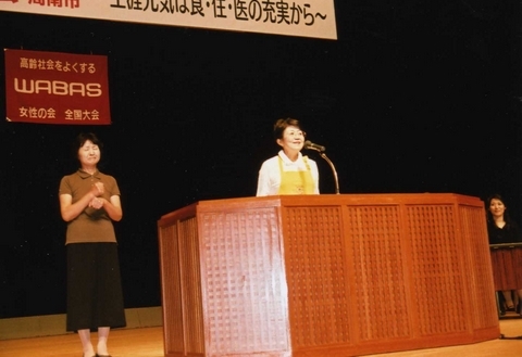 笑顔で開会宣言をする長谷川和美大会実行委員長。黄色いエプロン姿（実行委員会の制服）が新鮮